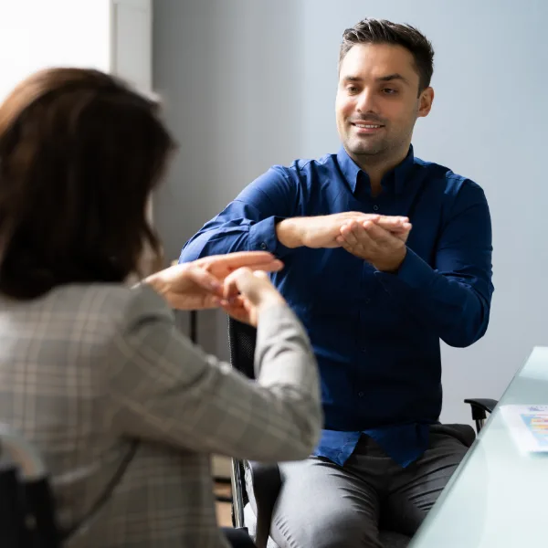 Learn Auslan R 2 A man and a woman sit across from each other at a desk, communicating using sign language.